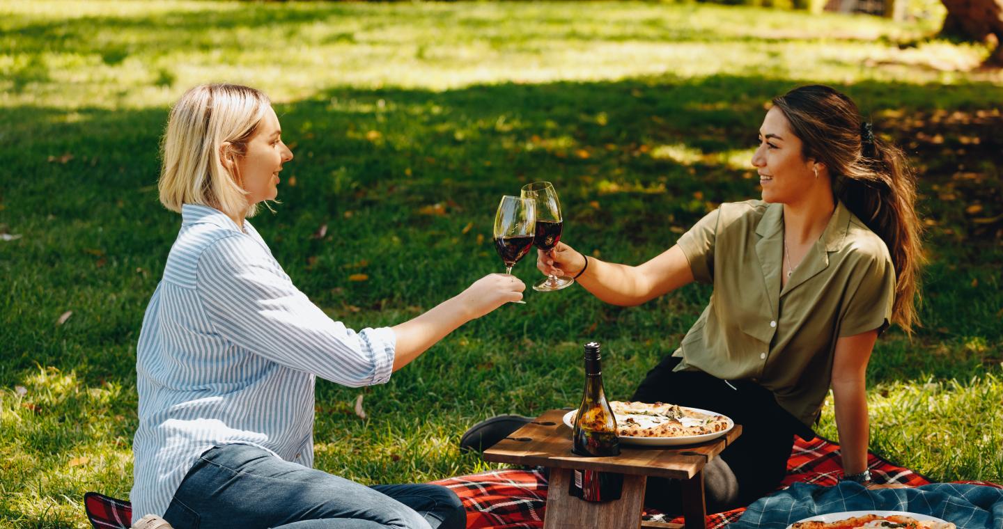 two adults seated on the lawn at Shadowfax Winery with pizza and wine