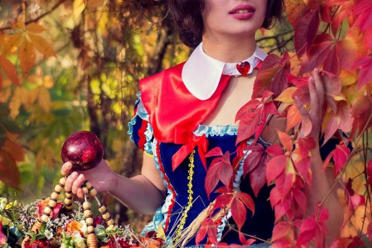 An actress dressed as Snow White in front of autumn trees holding a basket