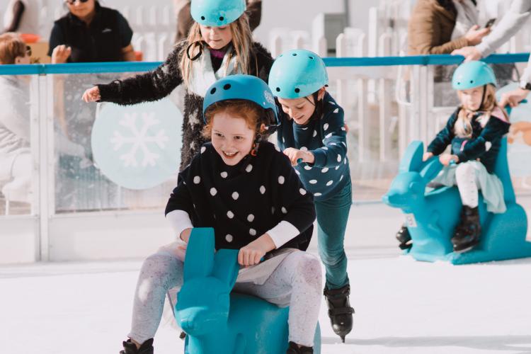 children wearing ice skates using kangaroo skating aid