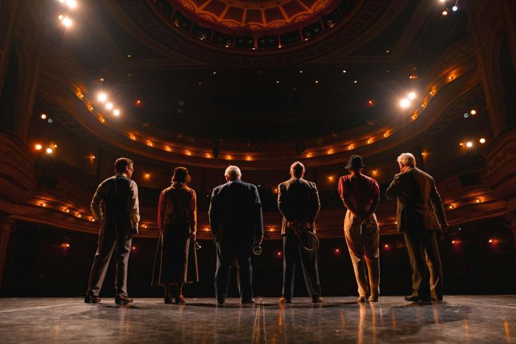 Six actors standing on a stage in a theatre