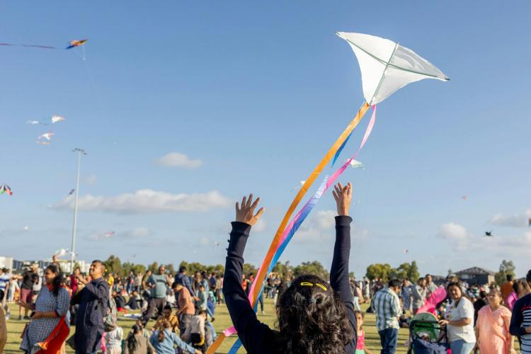 adult with hands in air throwing up kite with hundreds of people flying kites in front of them