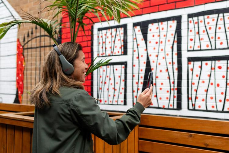 adult wearing headphones and holding out phone in front of street art