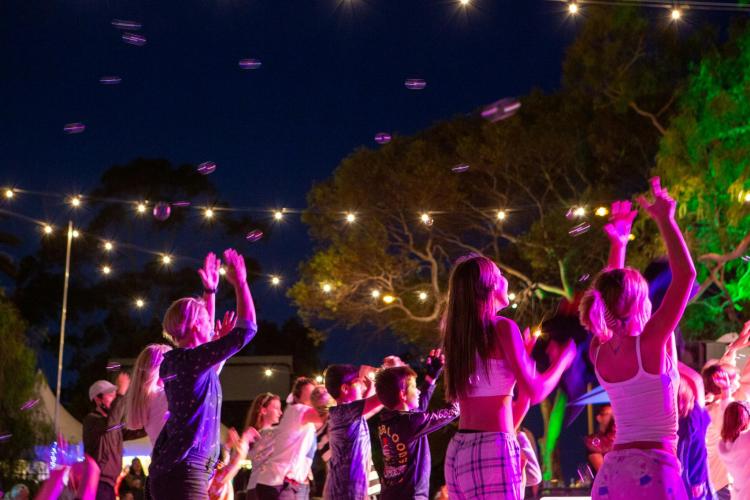 audience dancing at night beneath festoon lighting in park