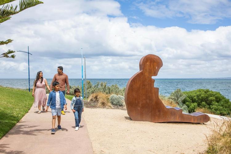 two adults and two children walking on path by sculpture and ocean